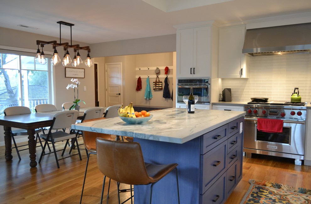 Design ideas for a large country l-shaped open plan kitchen in San Francisco with an undermount sink, shaker cabinets, white cabinets, granite benchtops, white splashback, ceramic splashback, stainless steel appliances, medium hardwood floors, with island, brown floor and blue benchtop.
