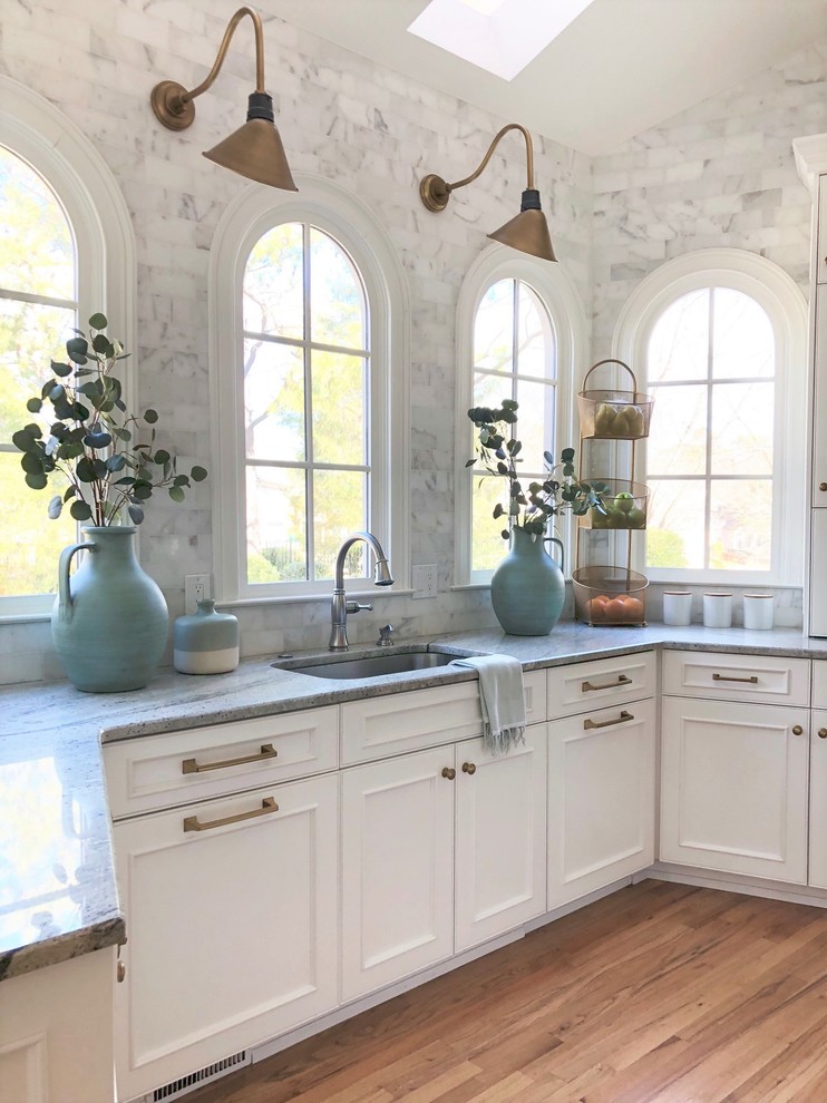 Photo of a large transitional l-shaped eat-in kitchen in Atlanta with an undermount sink, beaded inset cabinets, white cabinets, granite benchtops, white splashback, marble splashback, stainless steel appliances, light hardwood floors and with island.