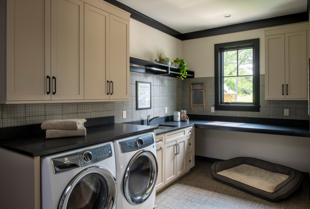 Photo of a mid-sized country l-shaped dedicated laundry room in Minneapolis with an undermount sink, recessed-panel cabinets, beige cabinets, granite benchtops, multi-coloured splashback, ceramic splashback, beige walls, vinyl floors, a side-by-side washer and dryer, multi-coloured floor and black benchtop.