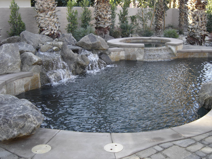Inspiration for a mid-sized tropical backyard custom-shaped natural pool in Orange County with brick pavers and a hot tub.