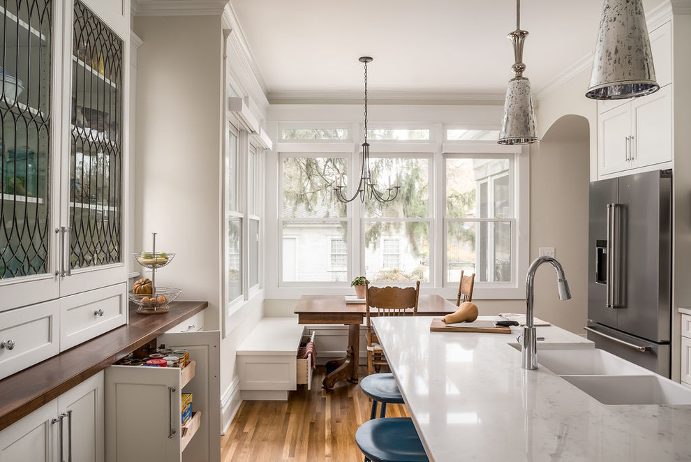 Large transitional u-shaped medium tone wood floor and brown floor eat-in kitchen photo in Columbus with a farmhouse sink, shaker cabinets, white cabinets, quartz countertops, white backsplash, marble backsplash, stainless steel appliances, an island and white countertops