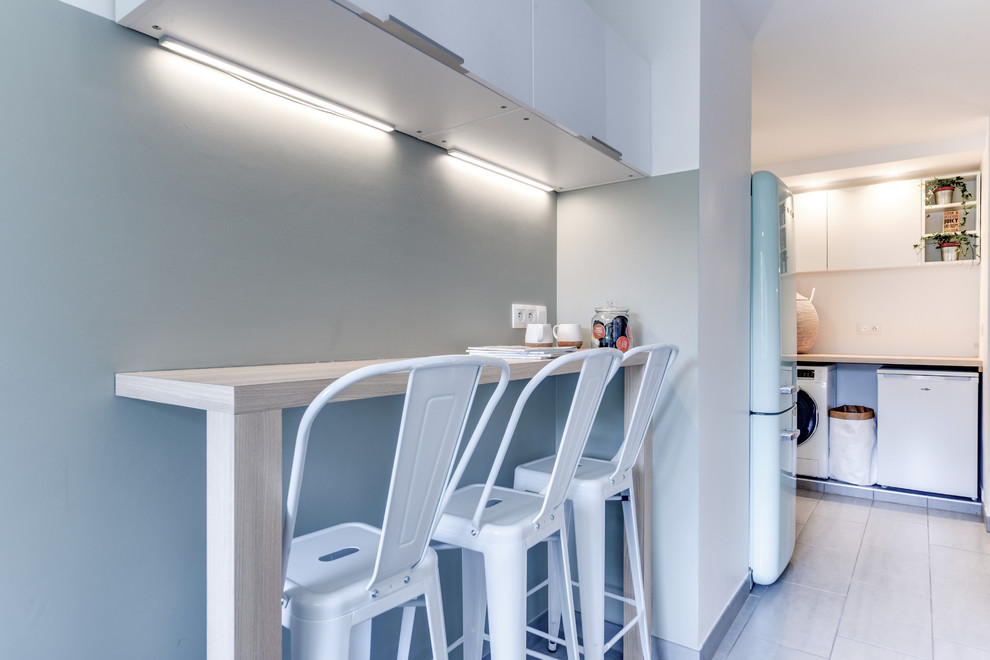 This is an example of a small contemporary l-shaped separate kitchen in Paris with an undermount sink, white cabinets, wood benchtops, white splashback, ceramic splashback, white appliances, ceramic floors and grey floor.