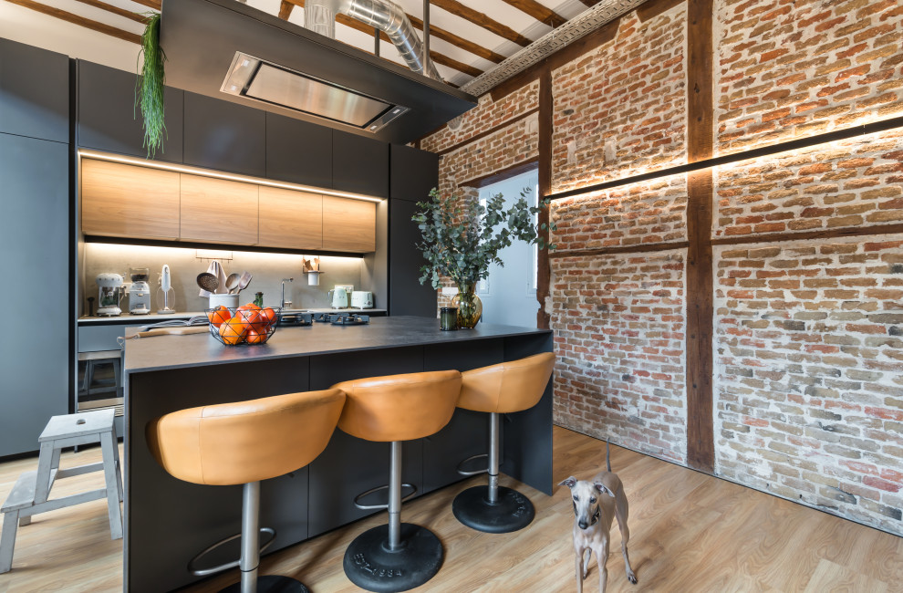 Photo of an industrial galley kitchen in Madrid with flat-panel cabinets, black cabinets, grey splashback, integrated appliances, light hardwood flooring, an island, beige floors, grey worktops and exposed beams.