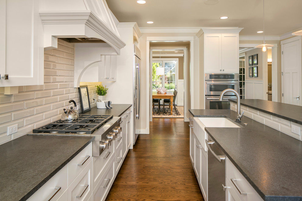 Inspiration for a timeless galley medium tone wood floor eat-in kitchen remodel in Seattle with a farmhouse sink, shaker cabinets, white cabinets, granite countertops, gray backsplash, subway tile backsplash, stainless steel appliances and an island