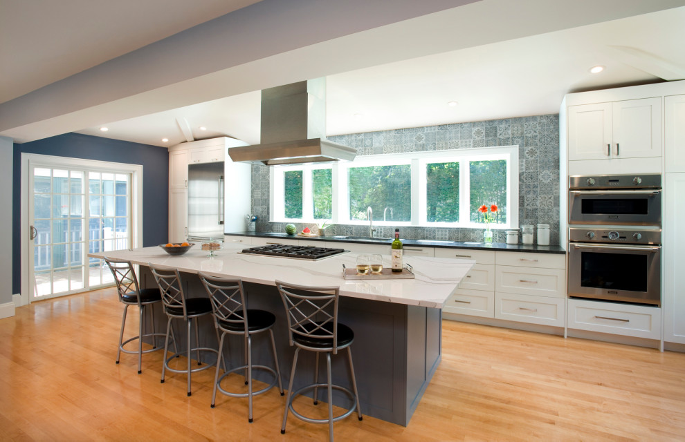 This is an example of a mid-sized modern single-wall separate kitchen in Boston with an undermount sink, shaker cabinets, white cabinets, granite benchtops, grey splashback, porcelain splashback, stainless steel appliances, light hardwood floors, with island, brown floor and multi-coloured benchtop.