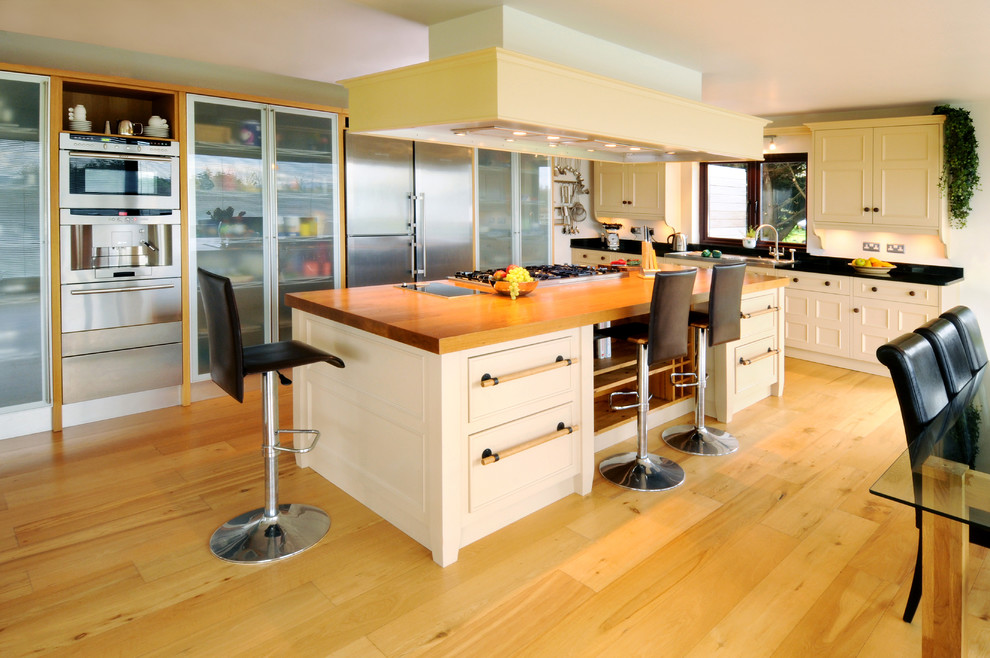 This is an example of a contemporary eat-in kitchen in Other with wood benchtops, glass-front cabinets and stainless steel appliances.