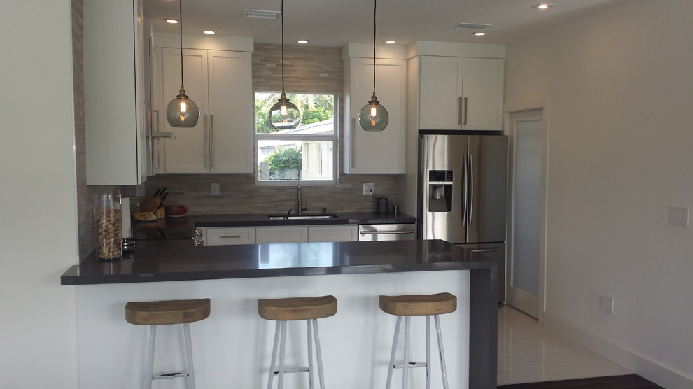 This is an example of a mid-sized modern u-shaped eat-in kitchen in Miami with an undermount sink, shaker cabinets, white cabinets, quartz benchtops, beige splashback, stone tile splashback, stainless steel appliances, porcelain floors and a peninsula.