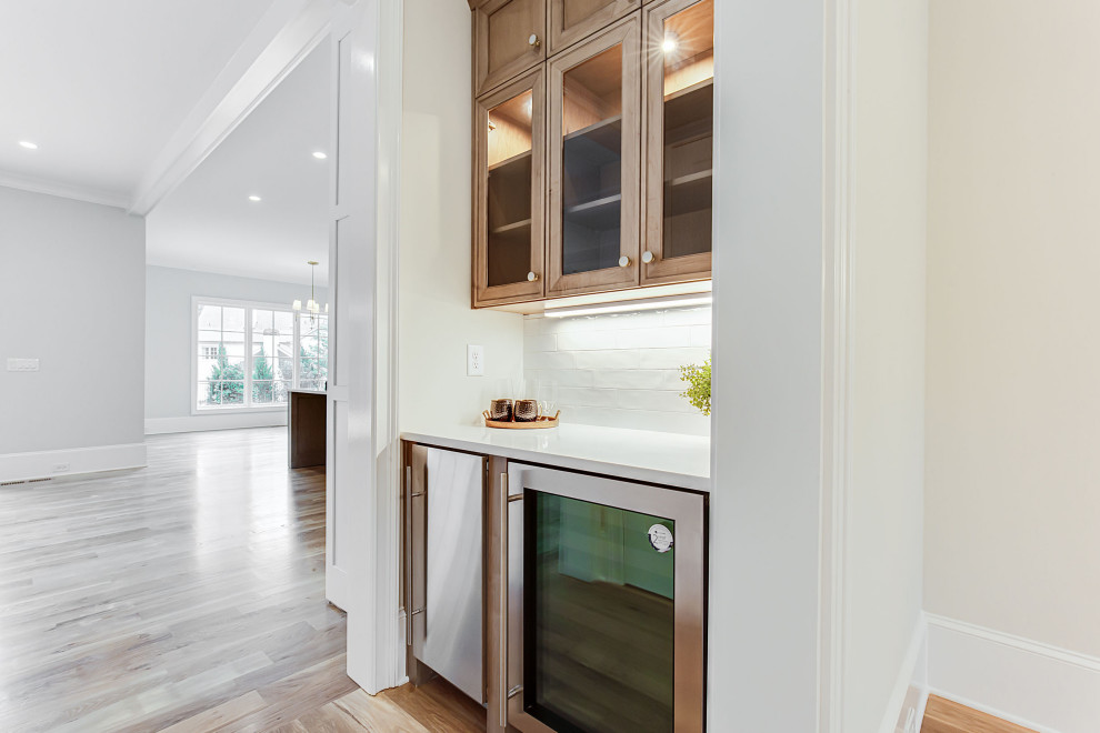 Klassisk inredning av ett stort vit vitt kök, med en undermonterad diskho, luckor med profilerade fronter, vita skåp, bänkskiva i kvarts, vitt stänkskydd, stänkskydd i tunnelbanekakel, integrerade vitvaror, mellanmörkt trägolv, en köksö och beiget golv