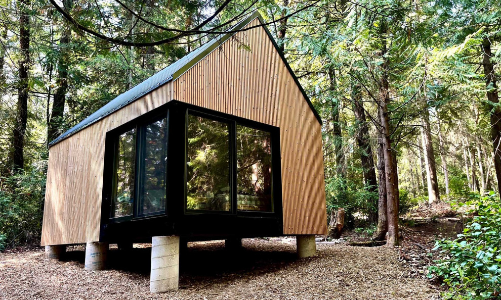 Foto på ett litet minimalistiskt brunt trähus, med allt i ett plan, sadeltak och tak i metall
