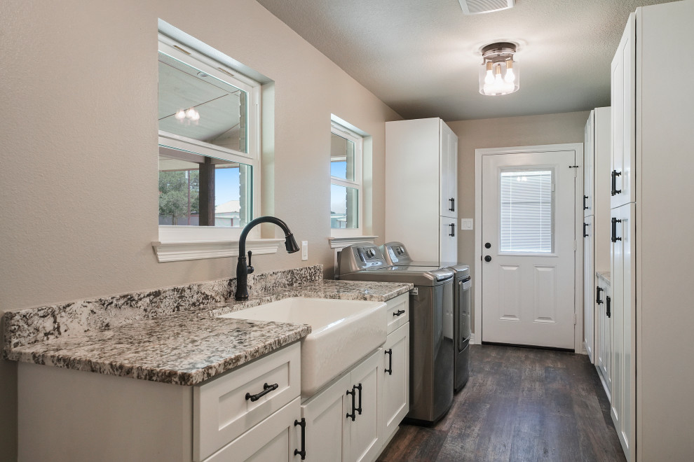Photo of a large arts and crafts laundry room in Houston with a farmhouse sink, shaker cabinets, distressed cabinets, granite benchtops, beige splashback, porcelain splashback, dark hardwood floors, brown floor and brown benchtop.