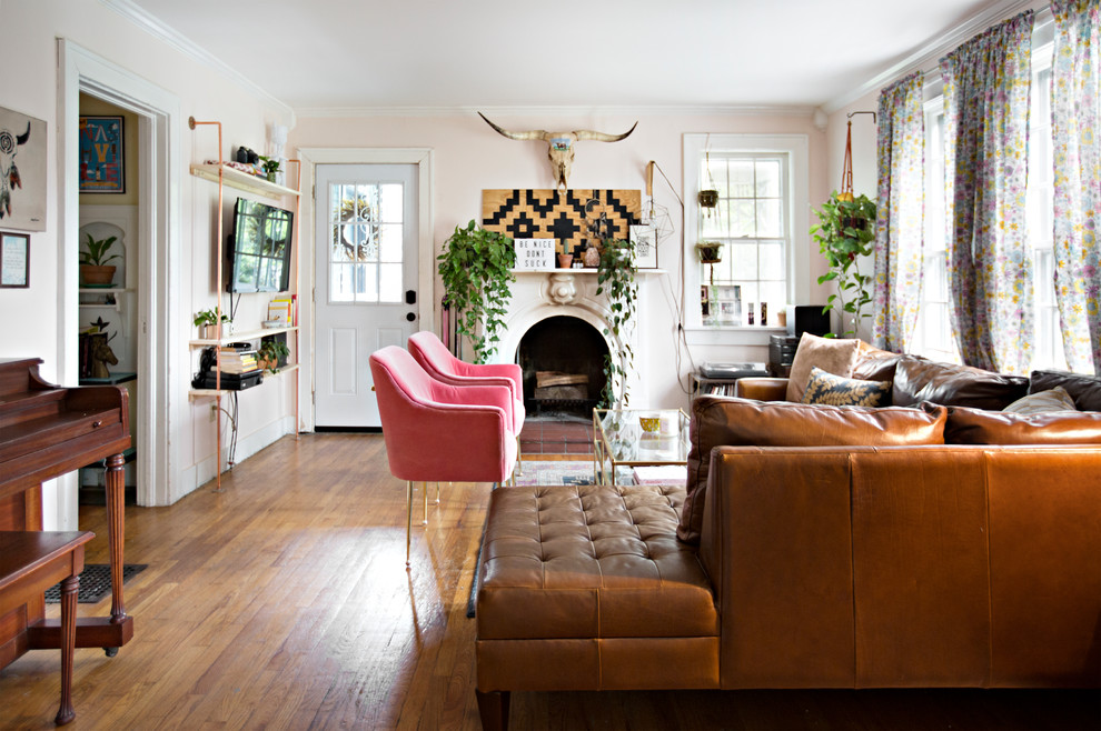 Photo of an eclectic enclosed living room in Nashville with pink walls, medium hardwood floors, a standard fireplace, a plaster fireplace surround, a wall-mounted tv and brown floor.