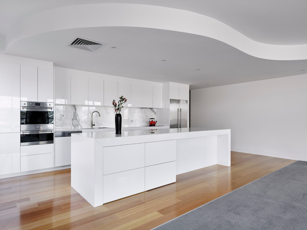 Design ideas for a large modern open plan kitchen in Other with a double-bowl sink, white cabinets, solid surface benchtops, white splashback, stainless steel appliances, medium hardwood floors, with island, flat-panel cabinets, porcelain splashback and white benchtop.
