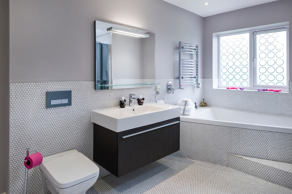Inspiration for a contemporary bathroom in West Midlands with an integrated sink, flat-panel cabinets, dark wood cabinets, a drop-in tub, a wall-mount toilet, white tile, mosaic tile, grey walls and mosaic tile floors.