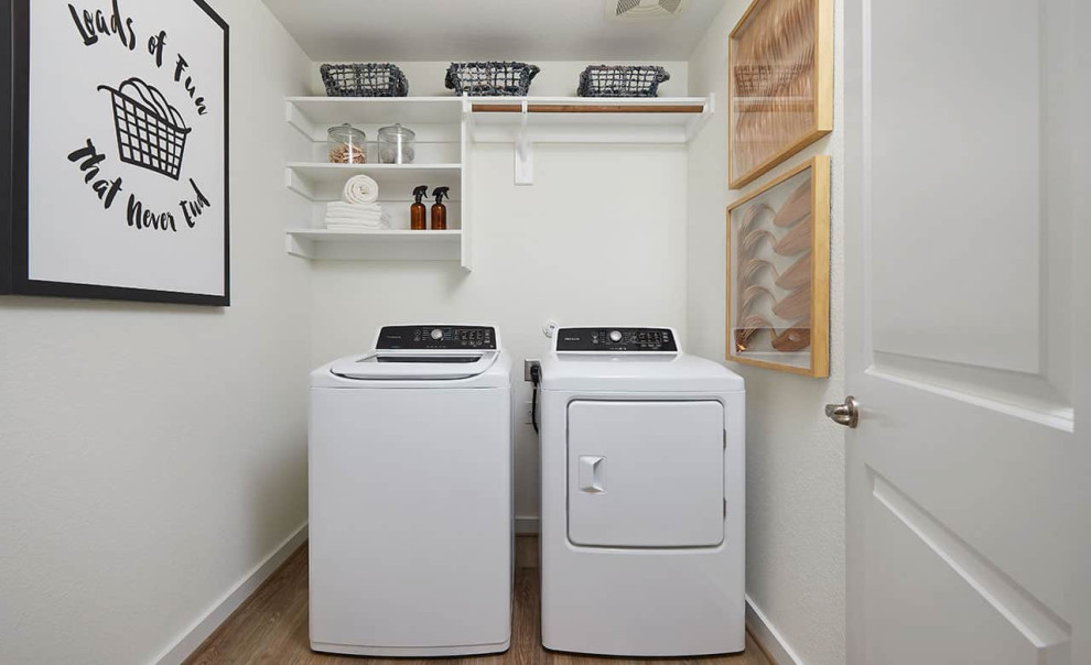 Esempio di una sala lavanderia contemporanea con pareti bianche, pavimento in laminato, lavatrice e asciugatrice affiancate e pavimento marrone