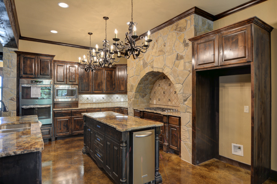 Eat-in kitchen - mid-sized rustic concrete floor eat-in kitchen idea with an undermount sink, raised-panel cabinets, dark wood cabinets, granite countertops, beige backsplash, stone tile backsplash, stainless steel appliances and an island