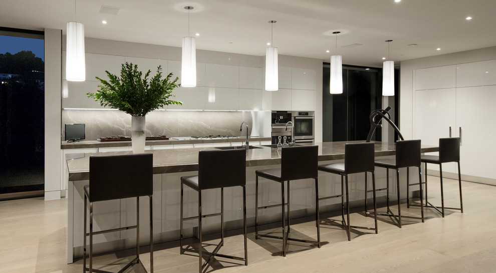 This is an example of a contemporary galley kitchen in Los Angeles with flat-panel cabinets, white cabinets, grey splashback, stainless steel appliances, light hardwood floors, with island and stone slab splashback.