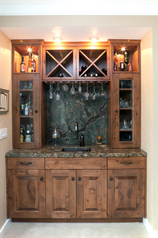This is an example of a small country single-wall wet bar in Seattle with an undermount sink, raised-panel cabinets, medium wood cabinets, granite benchtops, multi-coloured splashback, stone slab splashback and carpet.