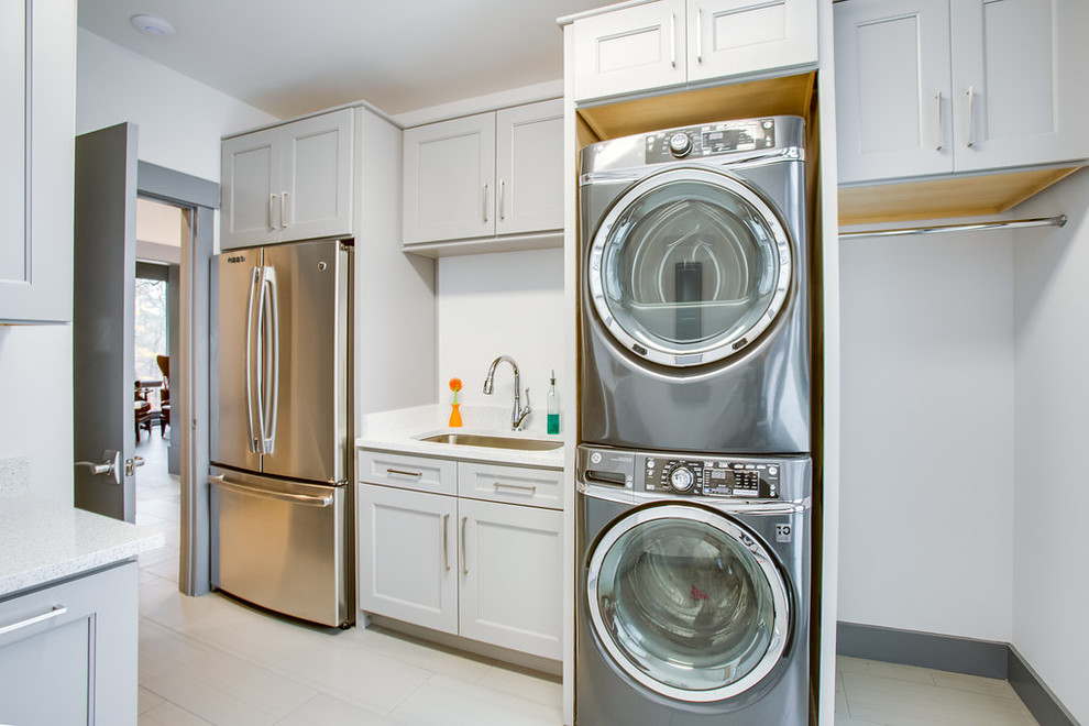 This is an example of a mid-sized modern utility room in Birmingham with an undermount sink, recessed-panel cabinets, grey cabinets, quartz benchtops, grey walls, ceramic floors, a stacked washer and dryer, beige floor and white benchtop.