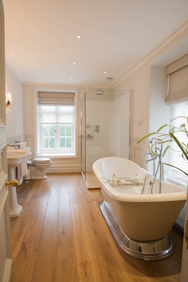 Large traditional kids bathroom in London with a freestanding tub, an open shower, a one-piece toilet, beige walls, light hardwood floors, a pedestal sink, brown floor and a sliding shower screen.