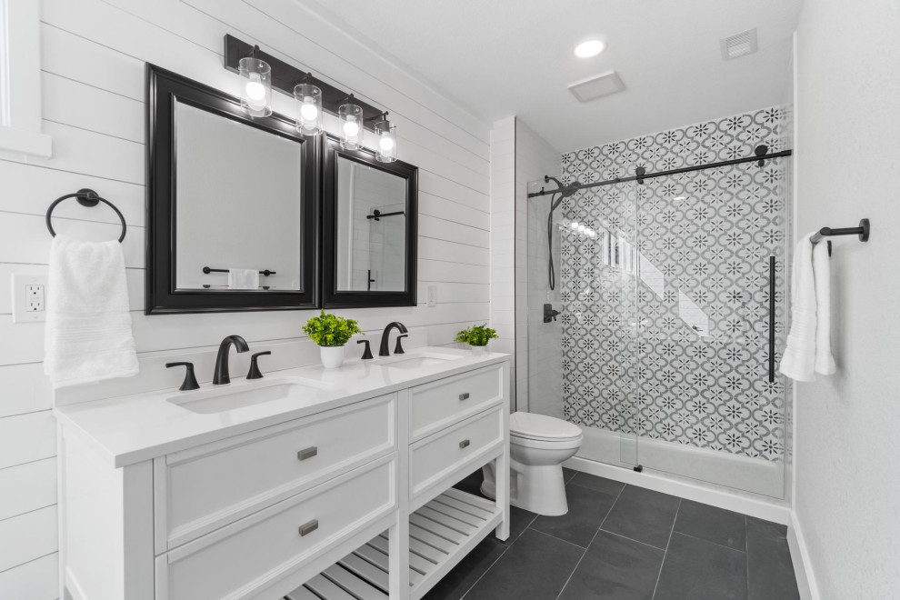 This is an example of a large midcentury master bathroom in San Diego with furniture-like cabinets, white cabinets, an alcove shower, a one-piece toilet, gray tile, white walls, an undermount sink, black floor, a sliding shower screen, white benchtops, a double vanity, a freestanding vanity, planked wall panelling, porcelain tile and engineered quartz benchtops.
