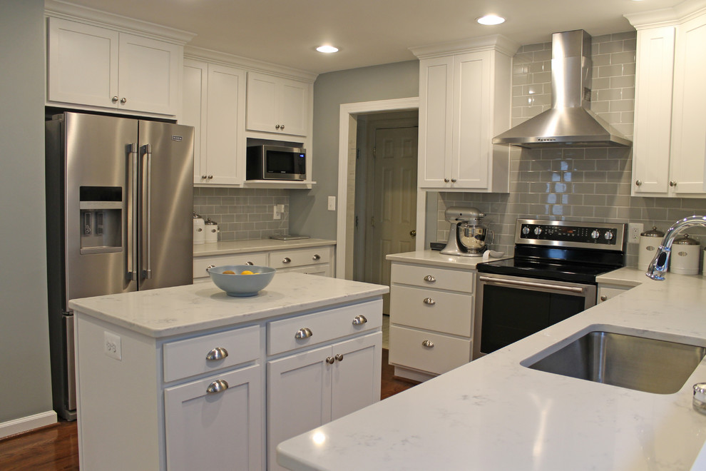 Photo of a mid-sized transitional u-shaped eat-in kitchen in Baltimore with an undermount sink, shaker cabinets, white cabinets, granite benchtops, grey splashback, subway tile splashback, stainless steel appliances, medium hardwood floors, with island, brown floor and white benchtop.