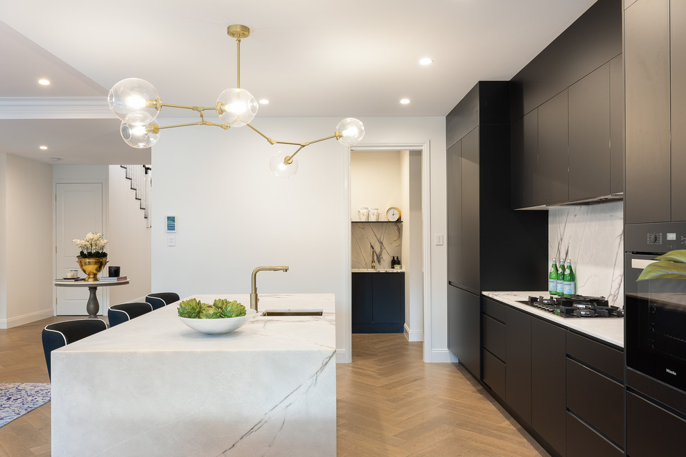 Photo of a contemporary single-wall kitchen in Brisbane with an undermount sink, flat-panel cabinets, black cabinets, white splashback, black appliances, medium hardwood floors, with island, brown floor and white benchtop.