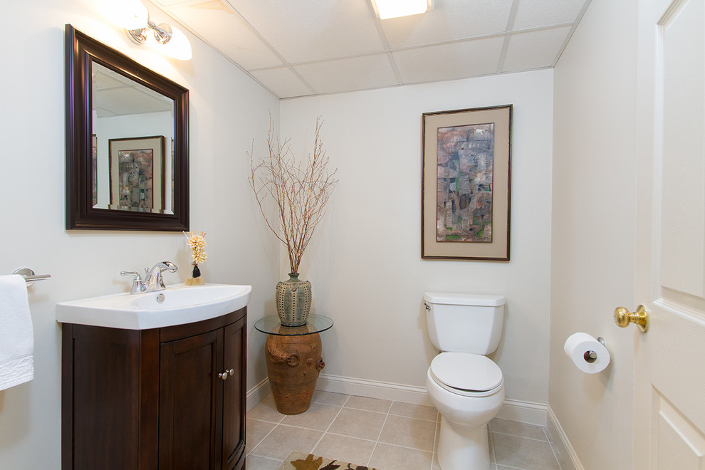 This is an example of a mid-sized traditional powder room in Providence with furniture-like cabinets, dark wood cabinets, a two-piece toilet, beige walls, ceramic floors, an integrated sink and beige floor.