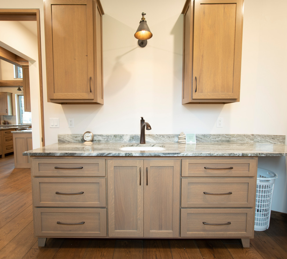 Example of a mountain style medium tone wood floor laundry room design with an undermount sink, shaker cabinets, light wood cabinets, quartz countertops, quartz backsplash and white walls