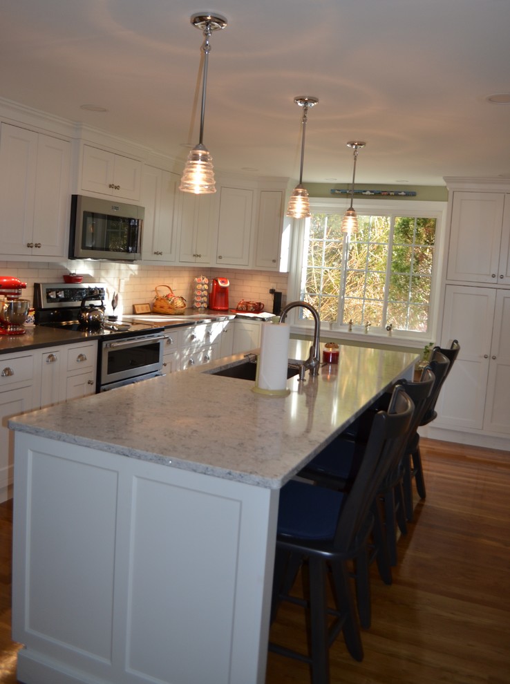 Example of a transitional l-shaped light wood floor eat-in kitchen design in Boston with an undermount sink, beaded inset cabinets, white cabinets, quartz countertops, white backsplash, ceramic backsplash, stainless steel appliances, an island and gray countertops