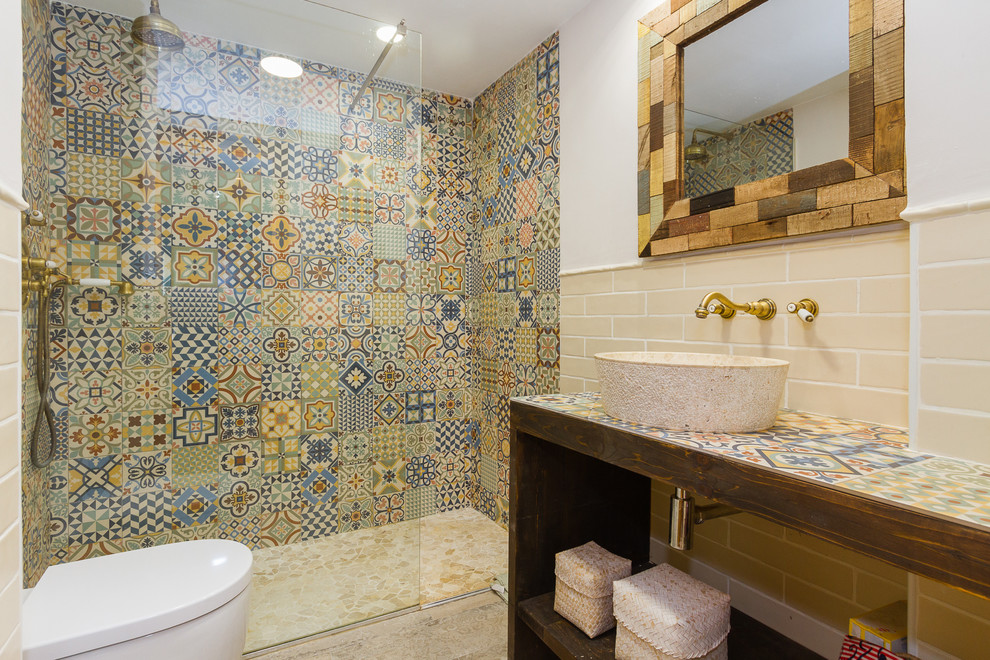 Design ideas for a mid-sized mediterranean master bathroom in Other with open cabinets, an alcove shower, a wall-mount toilet, multi-coloured tile, ceramic tile, multi-coloured walls, a vessel sink, tile benchtops, dark wood cabinets, beige floor, an open shower and multi-coloured benchtops.