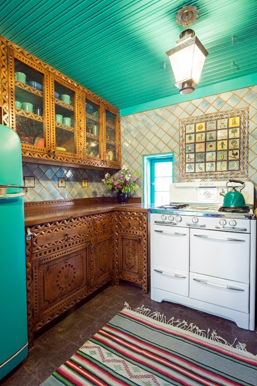 Photo of a mid-sized u-shaped kitchen in Albuquerque with a double-bowl sink, medium wood cabinets, multi-coloured splashback, no island, wood benchtops, terra-cotta splashback, coloured appliances and brick floors.
