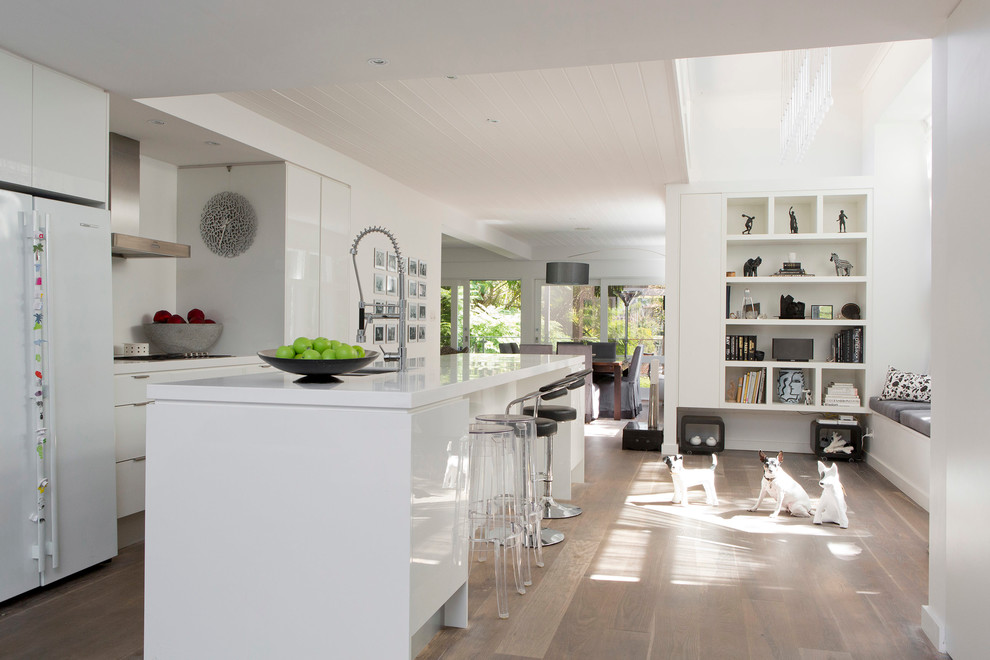 Mid-sized contemporary galley open plan kitchen in Sydney with an undermount sink, flat-panel cabinets, white cabinets, quartz benchtops, white splashback, glass sheet splashback, stainless steel appliances, light hardwood floors, with island, brown floor and white benchtop.