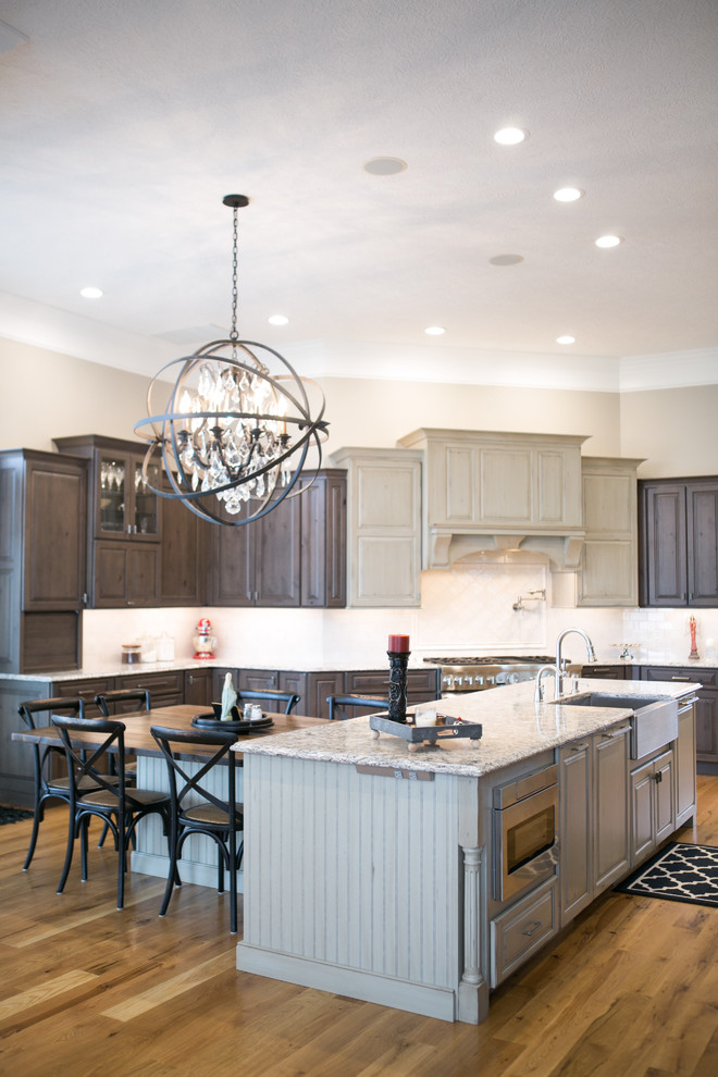 Example of a large transitional u-shaped medium tone wood floor and brown floor kitchen design in Indianapolis with a farmhouse sink, raised-panel cabinets, dark wood cabinets, granite countertops, white backsplash, subway tile backsplash, paneled appliances, an island and multicolored countertops
