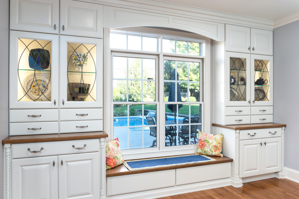 Example of a large transitional single-wall light wood floor and brown floor open concept kitchen design with a farmhouse sink, raised-panel cabinets, white cabinets, quartz countertops, white backsplash, ceramic backsplash, stainless steel appliances, an island and white countertops