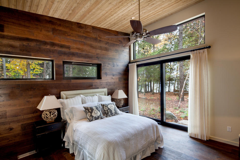 Inspiration for a large country master bedroom in Other with beige walls, dark hardwood floors, brown floor and a hanging fireplace.