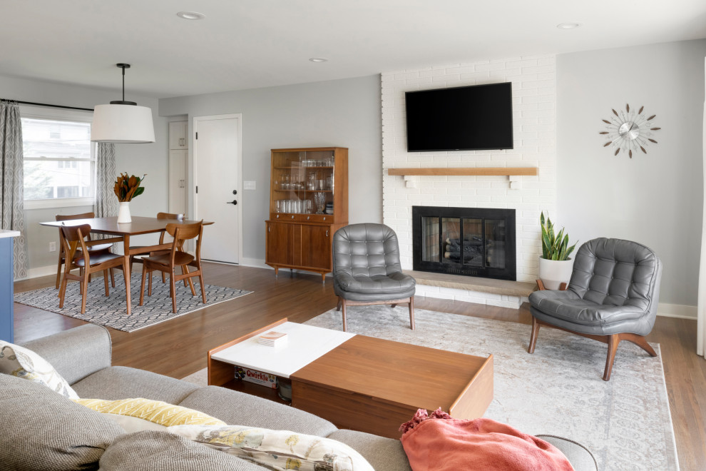 Design ideas for a large midcentury living room in Minneapolis with medium hardwood floors, a standard fireplace, a brick fireplace surround, brown floor and brick walls.