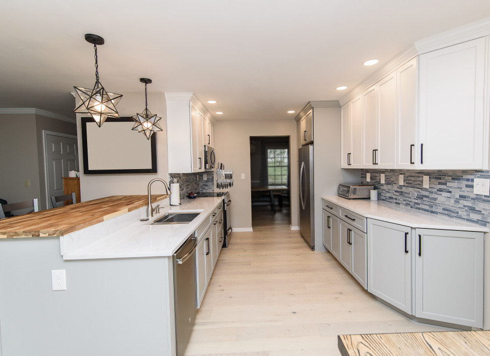 Example of a mid-sized transitional u-shaped enclosed kitchen design in Baltimore with an undermount sink, shaker cabinets, white cabinets, quartz countertops, blue backsplash, subway tile backsplash, stainless steel appliances, a peninsula and white countertops