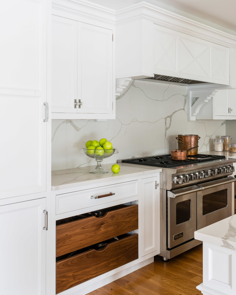 This is an example of a transitional kitchen in Boston with recessed-panel cabinets, white cabinets, quartz benchtops, white splashback, stone slab splashback, medium hardwood floors, brown floor and white benchtop.