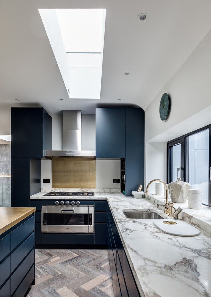 This is an example of a large modern u-shaped open plan kitchen in London with a drop-in sink, flat-panel cabinets, grey cabinets, copper benchtops, white splashback, marble splashback, stainless steel appliances, medium hardwood floors, a peninsula, brown floor and beige benchtop.