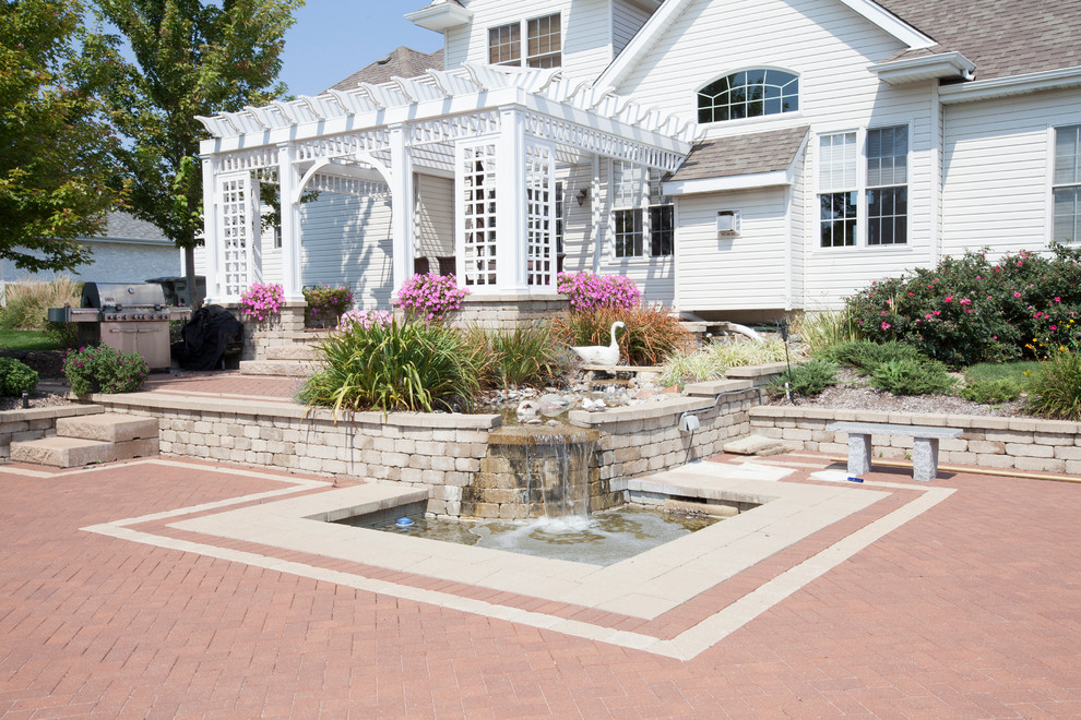 Mid-sized beach style backyard patio in Chicago with a water feature, brick pavers and a pergola.