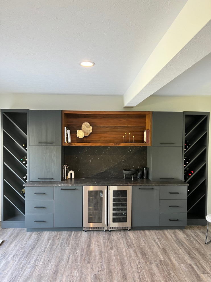 Design ideas for a large modern single-wall home bar in Indianapolis with shaker cabinets, black cabinets, black splashback, black benchtop, light hardwood floors and brown floor.