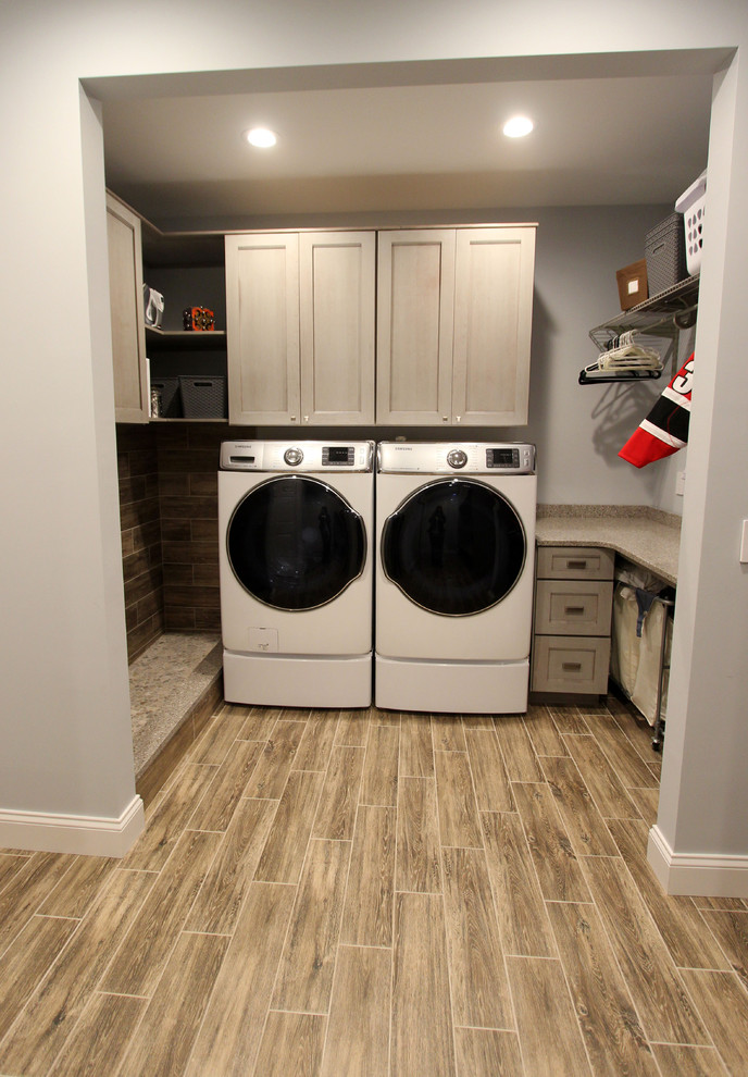 This is an example of a mid-sized transitional galley utility room with flat-panel cabinets, grey cabinets, quartz benchtops, grey walls, laminate floors, a side-by-side washer and dryer and brown floor.