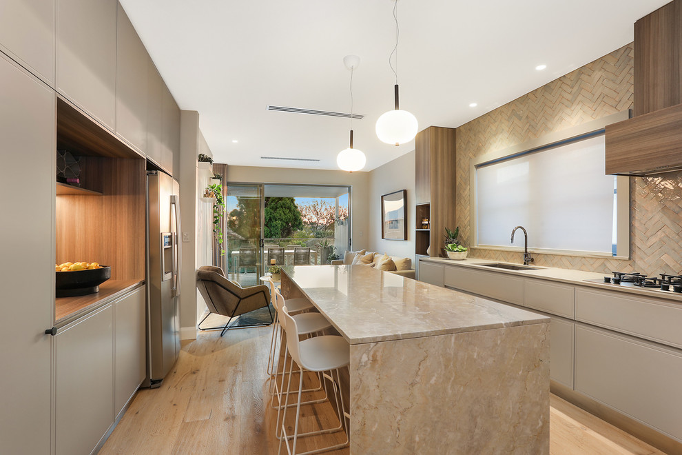 This is an example of a contemporary galley kitchen in Sydney with an undermount sink, flat-panel cabinets, grey cabinets, beige splashback, stainless steel appliances, light hardwood floors, with island, beige floor and beige benchtop.