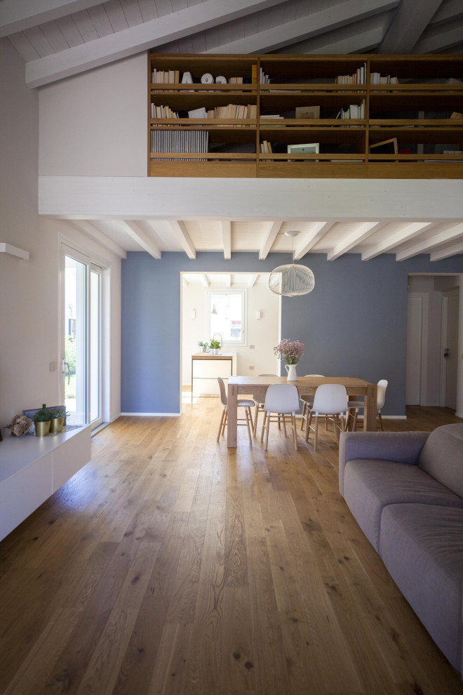 На фото: большая открытая гостиная комната в скандинавском стиле с с книжными шкафами и полками, синими стенами, паркетным полом среднего тона, бежевым полом и балками на потолке