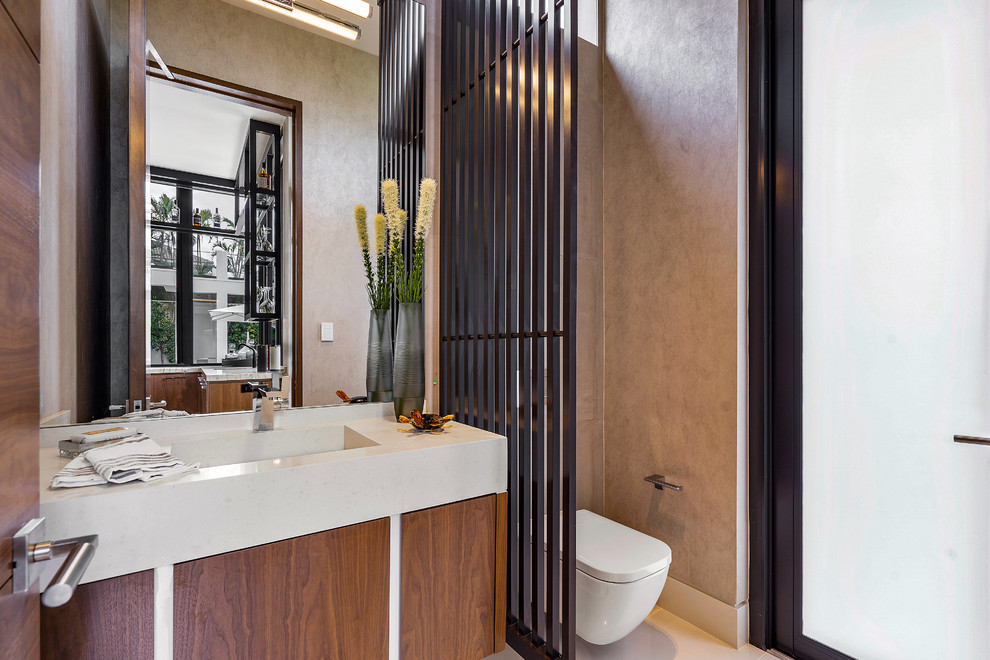 Design ideas for a large contemporary powder room in Miami with flat-panel cabinets, medium wood cabinets, a wall-mount toilet, brown walls, marble floors, an integrated sink, limestone benchtops, beige benchtops and beige floor.