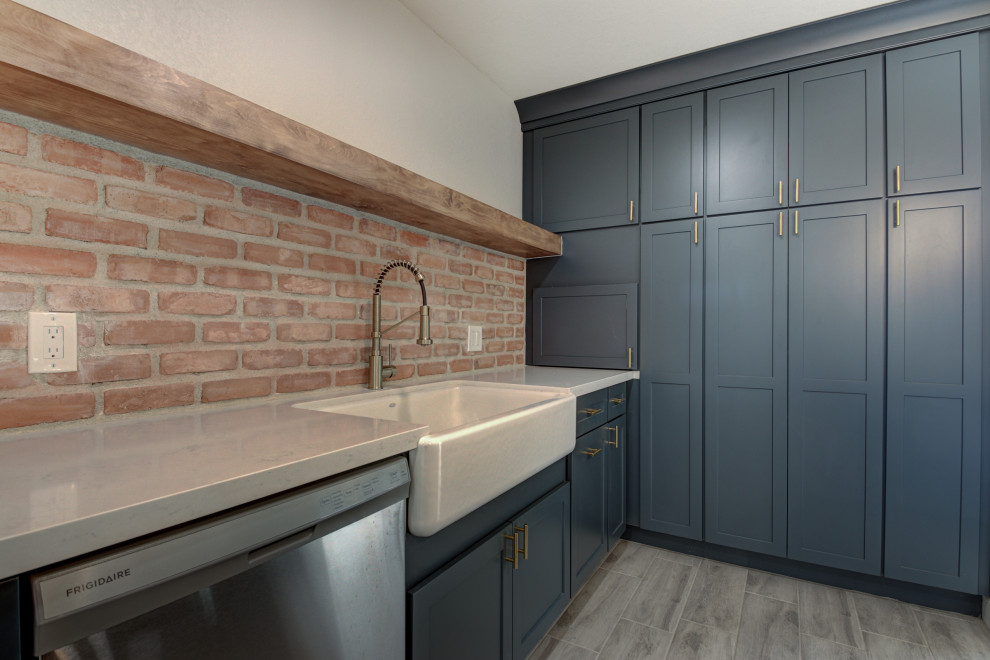 Eat-in kitchen - mid-sized transitional u-shaped porcelain tile and gray floor eat-in kitchen idea in Phoenix with a farmhouse sink, shaker cabinets, blue cabinets, quartz countertops, red backsplash, brick backsplash, stainless steel appliances, an island and white countertops