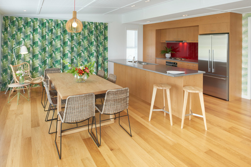 Inspiration for a mid-sized tropical galley eat-in kitchen in Auckland with a double-bowl sink, flat-panel cabinets, medium wood cabinets, quartz benchtops, red splashback, glass sheet splashback, stainless steel appliances, medium hardwood floors and with island.