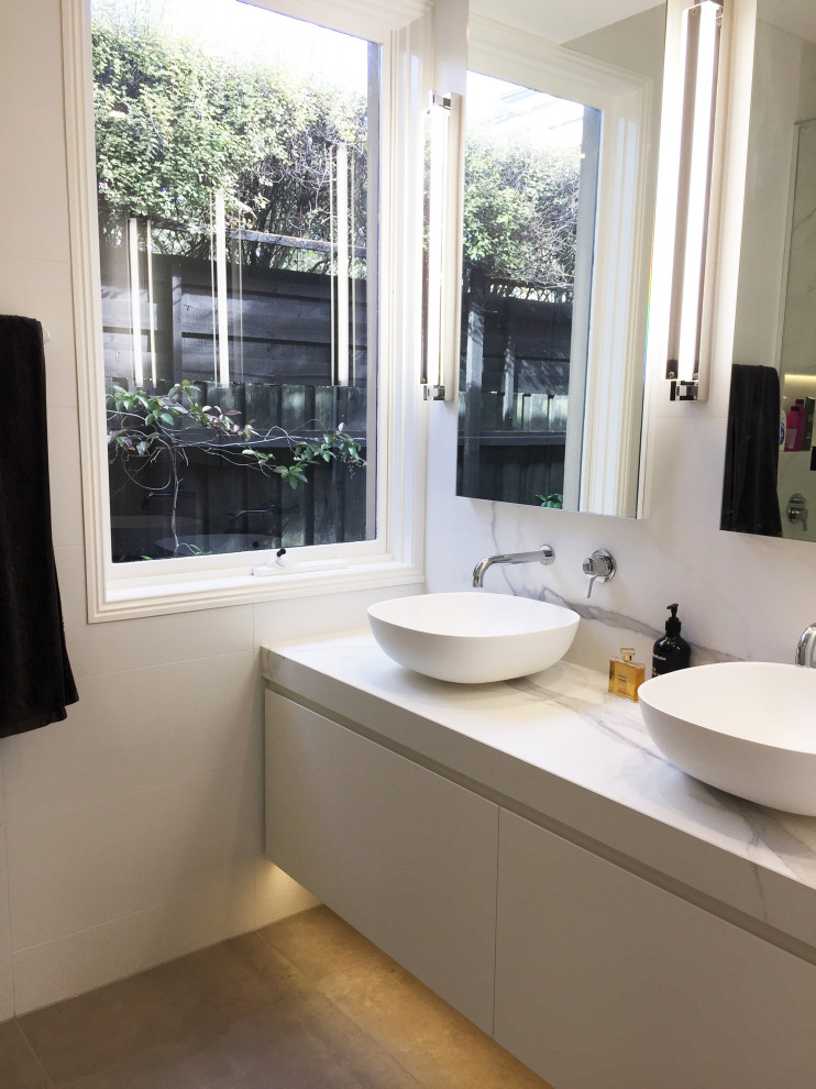 Photo of a mid-sized transitional master bathroom in Melbourne with flat-panel cabinets, white cabinets, a corner shower, a one-piece toilet, white tile, porcelain tile, white walls, porcelain floors, a vessel sink, brown floor, a hinged shower door and white benchtops.