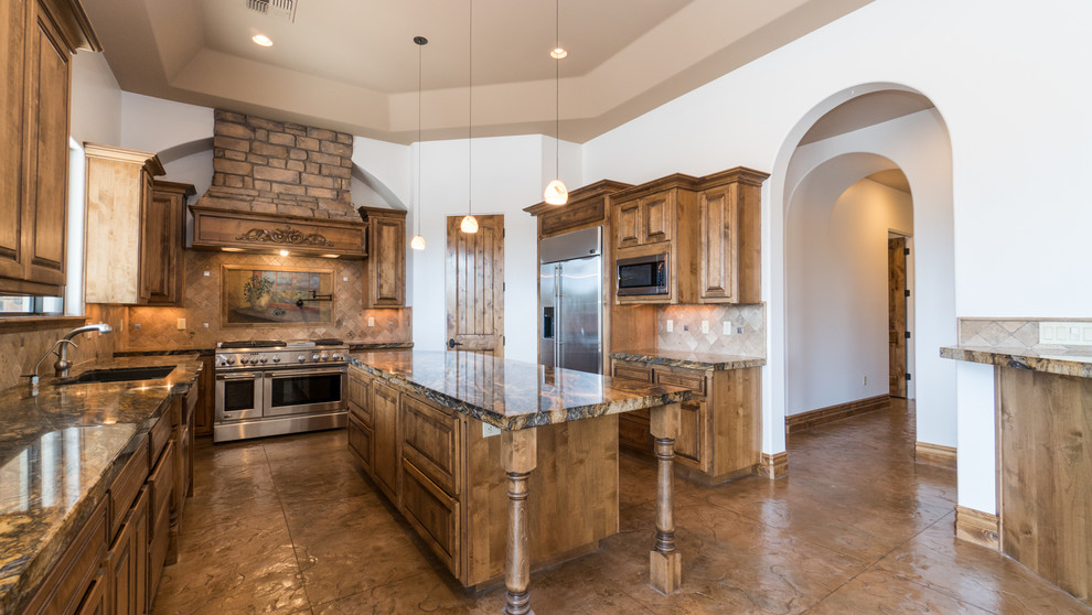 Inspiration for a large arts and crafts l-shaped separate kitchen in Phoenix with a drop-in sink, granite benchtops, beige splashback, stone tile splashback, stainless steel appliances, concrete floors, raised-panel cabinets, dark wood cabinets, with island and brown floor.