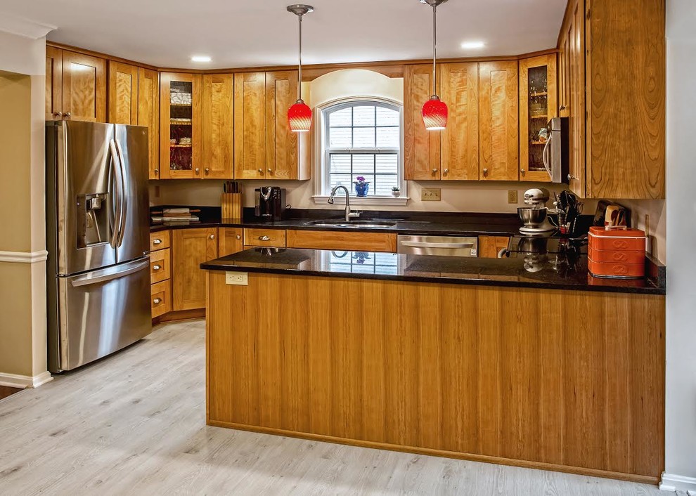 Traditional u-shaped eat-in kitchen in Baltimore with a double-bowl sink, shaker cabinets, medium wood cabinets, granite benchtops, stainless steel appliances, vinyl floors, a peninsula, grey floor and black benchtop.